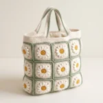 Cream daisy crochet tote bag with sage-green borders, yellow flower centers, twin handles and cream fabric lining