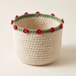 Round cream crochet storage basket with a green rim and small red crochet flowers