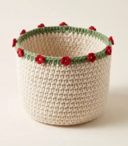 Round cream crochet storage basket with a green rim and small red crochet flowers